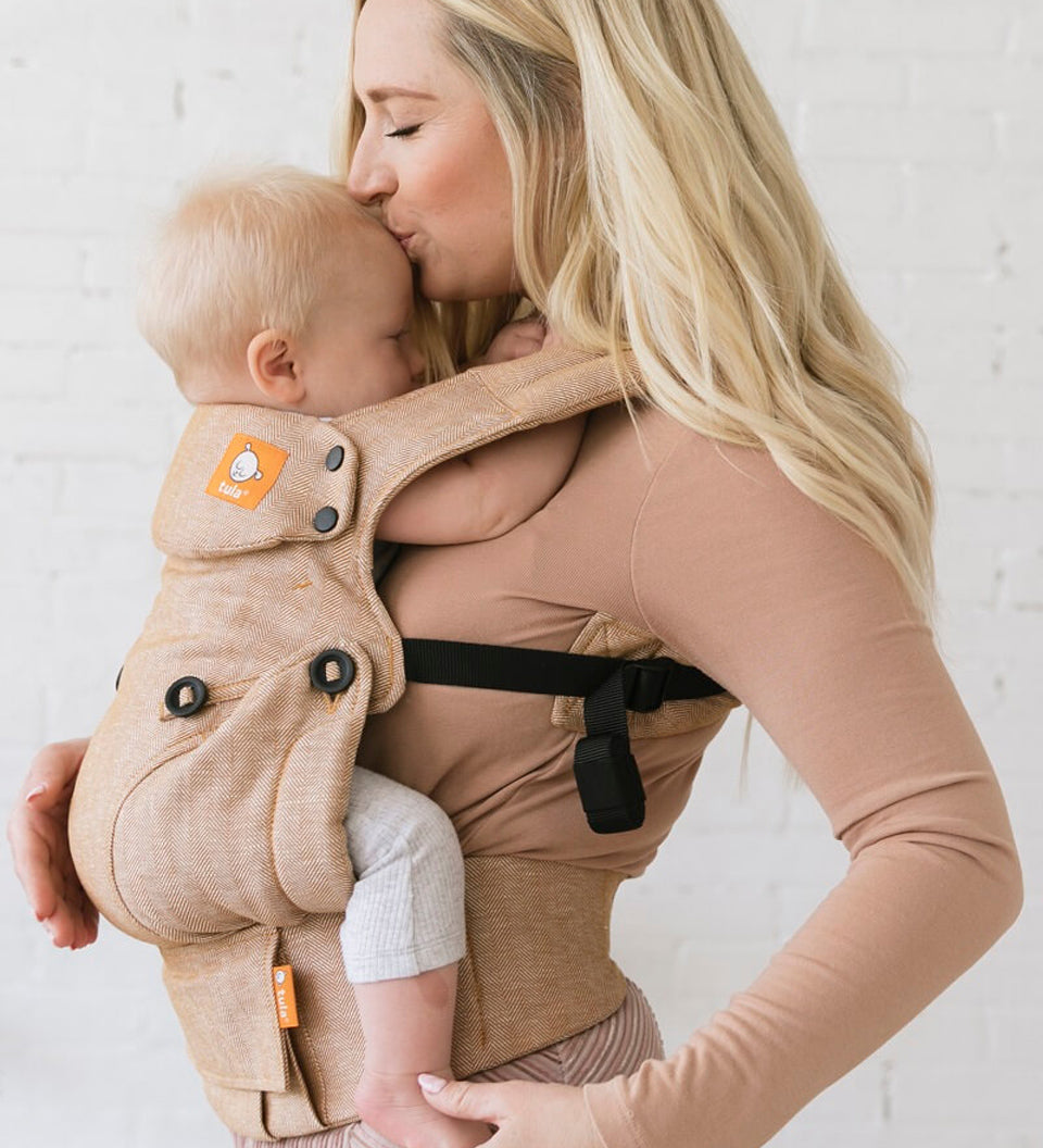 Close up of woman kissing a baby in a Tula explore front facing baby carrier