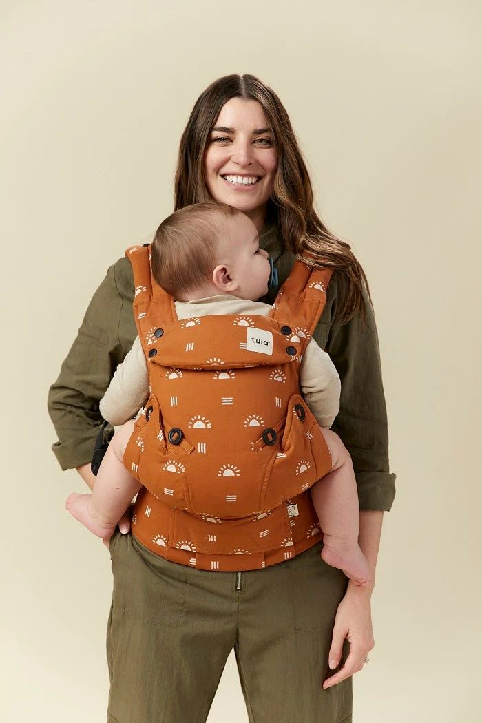 Front view of a woman carrying her baby on her front in the Tula Ergonomic Multi-Position Explore Baby Carrier 7-45lbs in Sedonia.