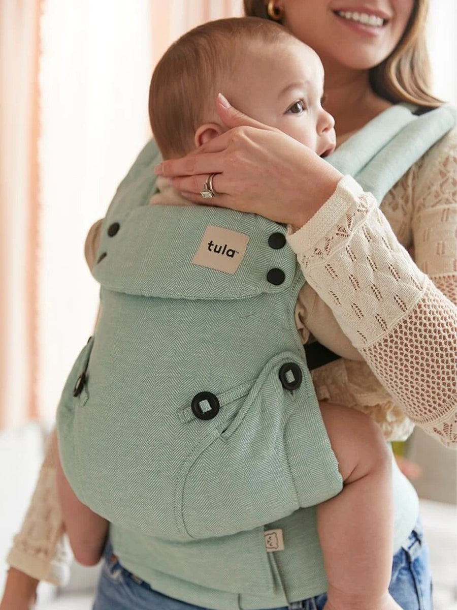 A baby is happily sat up in the Tula Explore Carrier