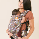 next to a boy carrying a white teddy bear in a Tula mini toy carrier in matching fox tail prints