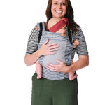 Woman stood on a white background carrying a baby in the Tula free to grow coast beyond baby carrier