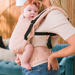 Close up of a baby in a Tula FTG stardust baby carrier in front of a blue sofa