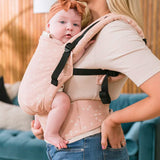 Close up of a baby in a Tula FTG stardust baby carrier in front of a blue sofa