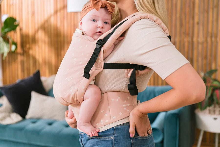 Close up of a baby in a Tula FTG stardust baby carrier in front of a blue sofa