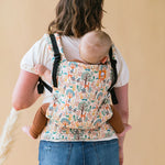 Close up of woman stood backwards with a baby on her back in a Tula free to grow charmed carrier