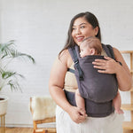 Woman stood holding a baby in a Tula organic cotton FTG baby carrier