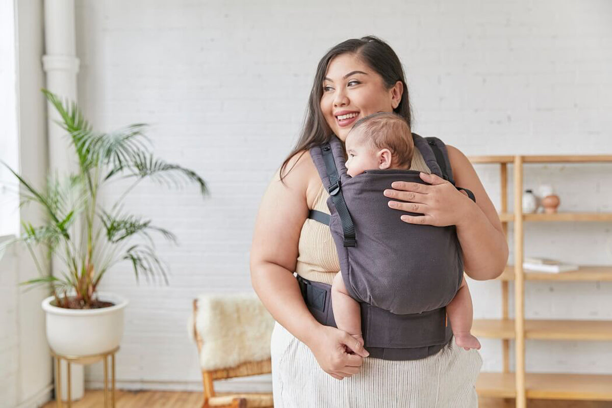 Woman stood holding a baby in a Tula organic cotton FTG baby carrier