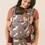 Man and woman stood in front of a white wall carrying two children in Tula fox tail print carriers