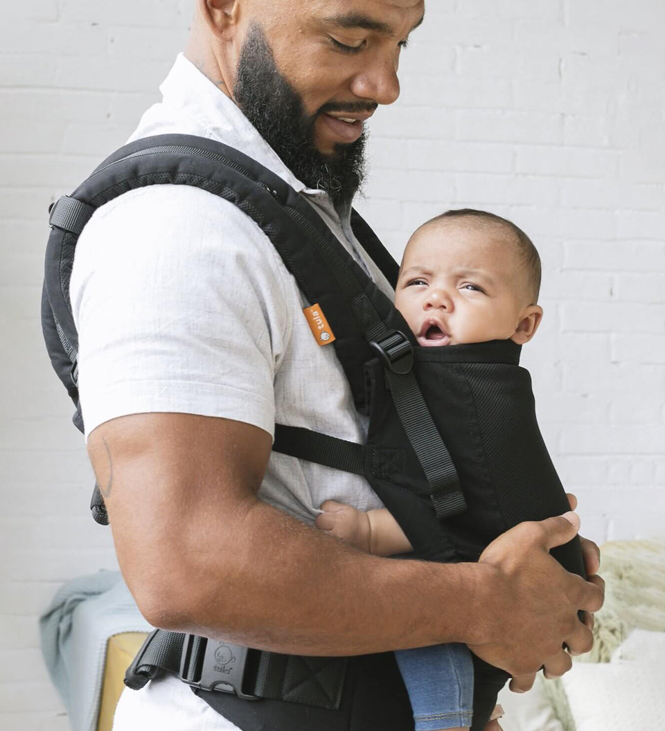 Woman stood holding a baby in a Tula FTG urbanista baby carrier