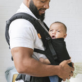 Woman stood holding a baby in a Tula FTG urbanista baby carrier