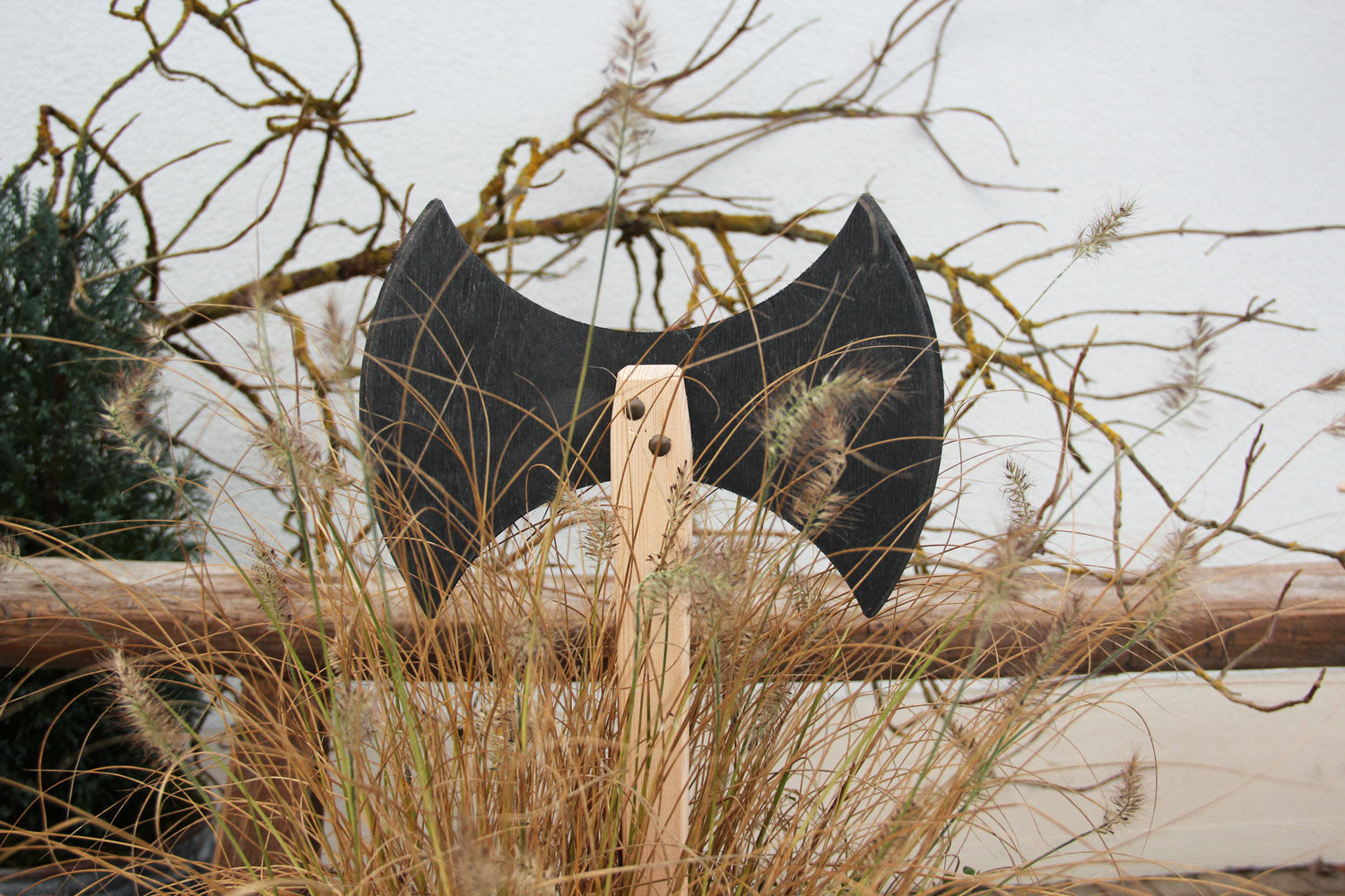 Vah Two-edged Wooden Viking Hatchet pictured outdoors placed against a fence behind reeds