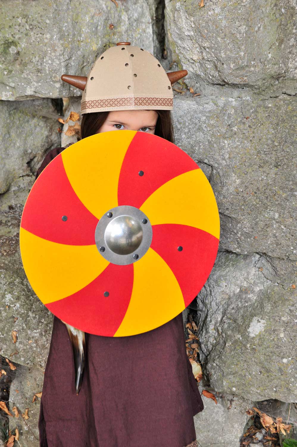 Child wearing a viking costume behind a Vah Grimwald Round Wooden Shield - Red & Yellow