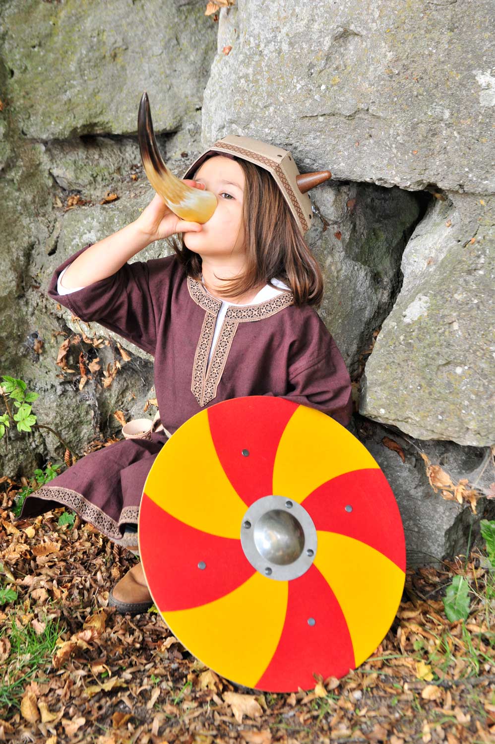 child wearing a viking costume. drinking from a drinking horn holding a Vah Grimwald Round Wooden Shield - Red & Yellow