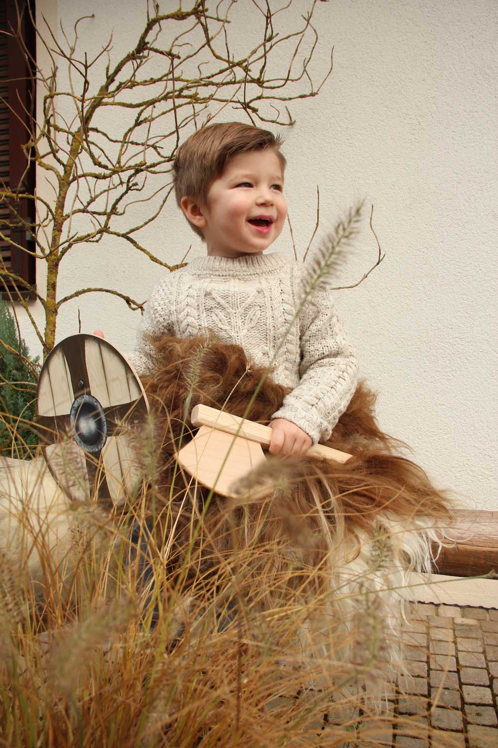 Child holding a Vah mini wooden axe in one hand and a round wooden shield in the other