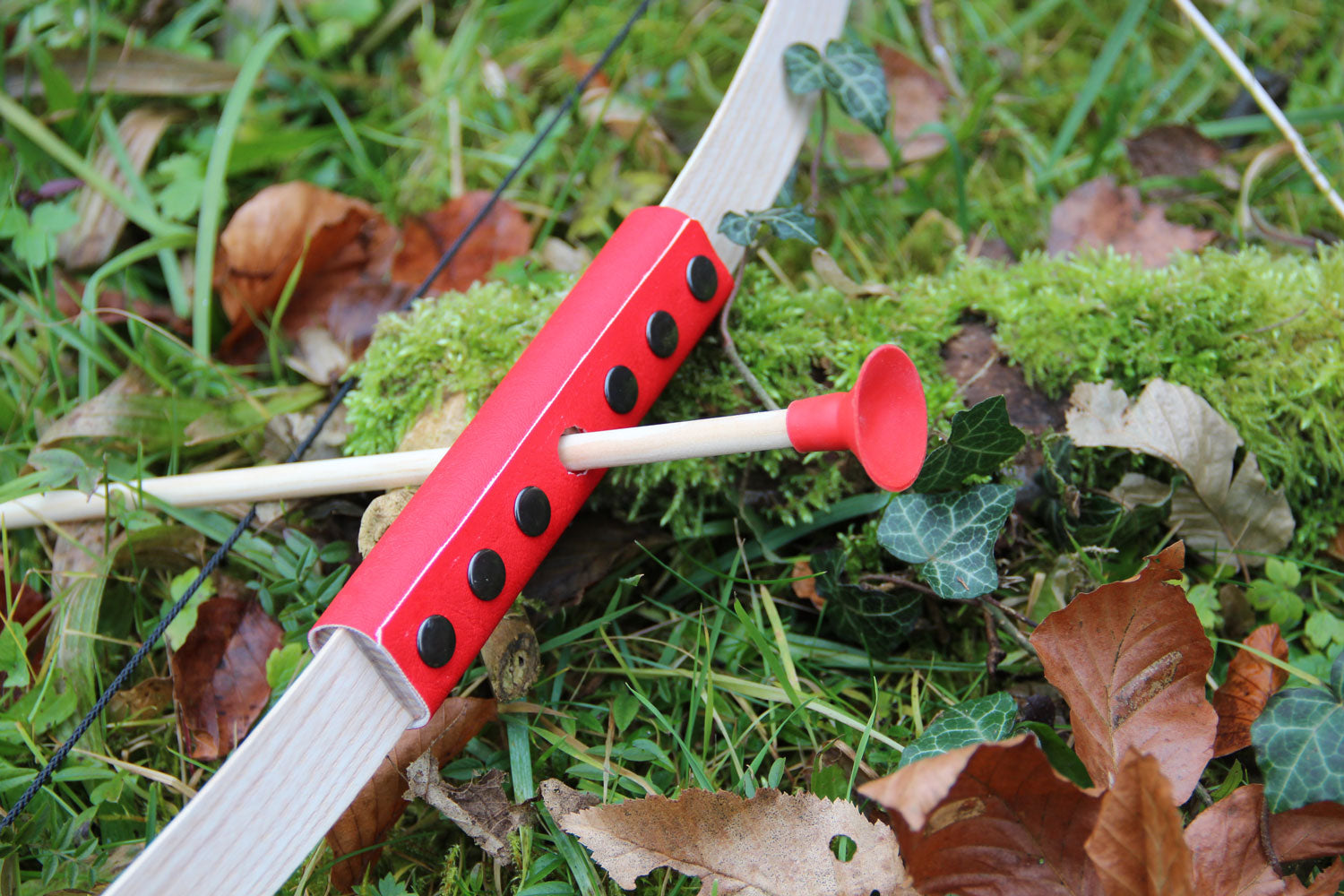 The Vah Mini Wooden Bow with Safety Arrows pictured on grass outdoors showing close up of arrow and red detail