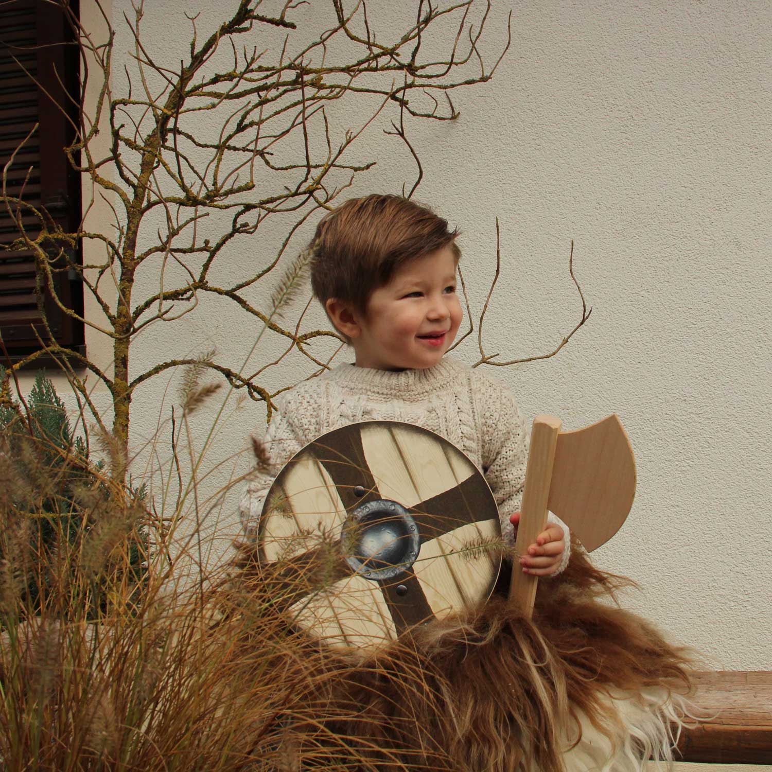 A child sitting outdoors holding the shield and axe from the Vah Ragnar Mini Wooden Shield & Axe Set