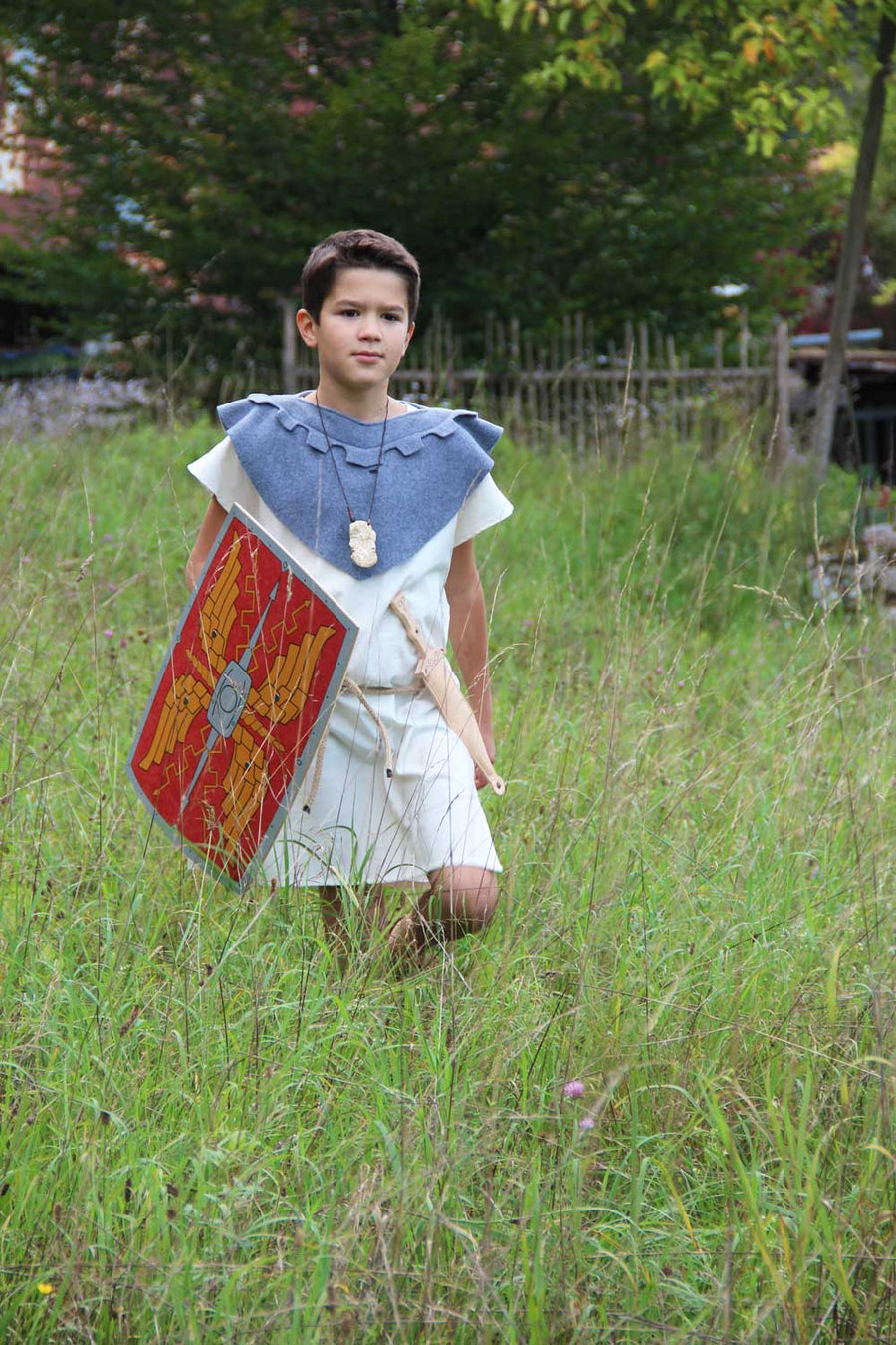 Child wearing a roman costume and carrying a Vah Roman Alexius Red Wooden Toy Shield