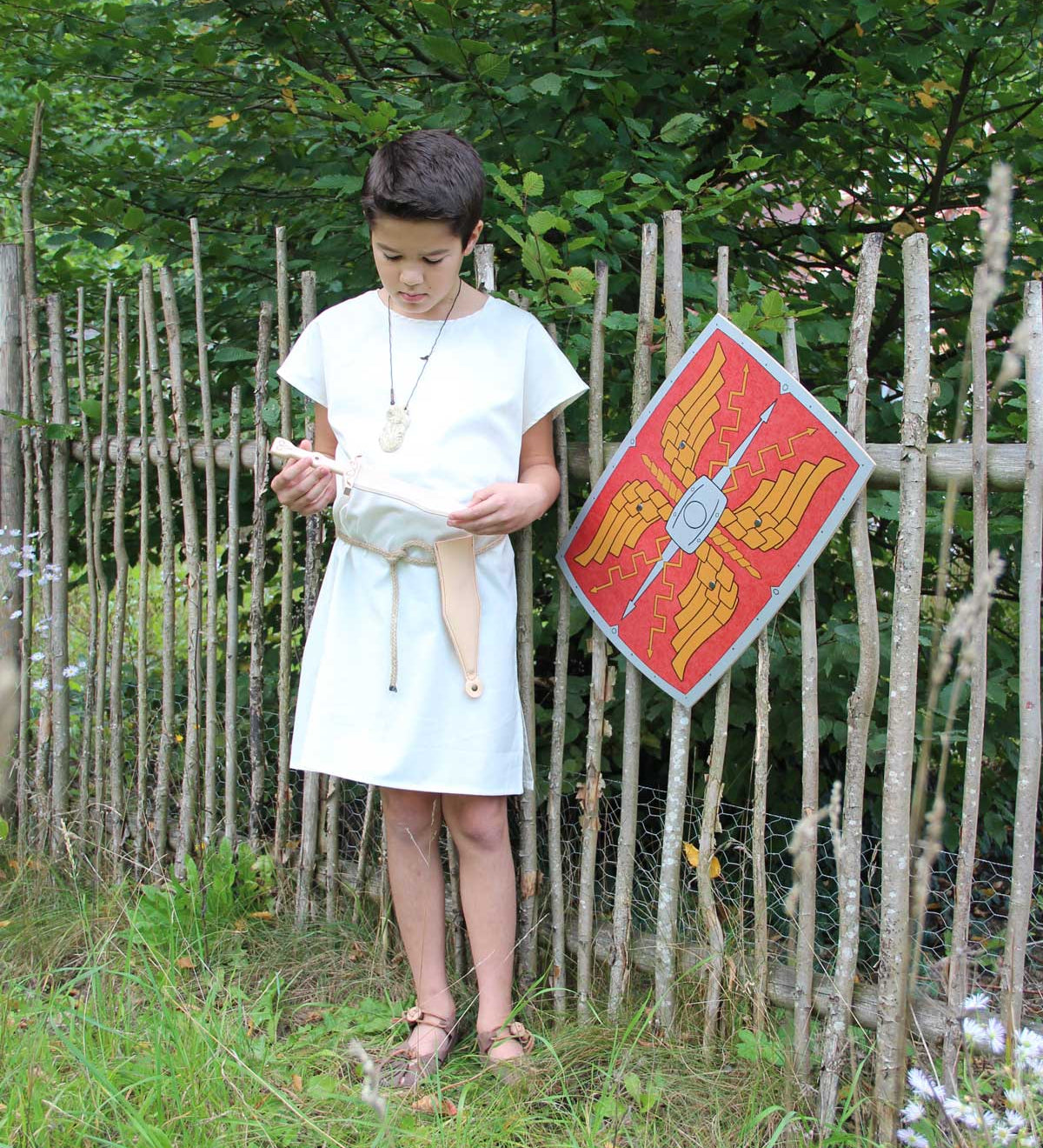 Child wearing the Vah Spartacus Roman Tunic with the red roman alexius shield placed on a fence next to them