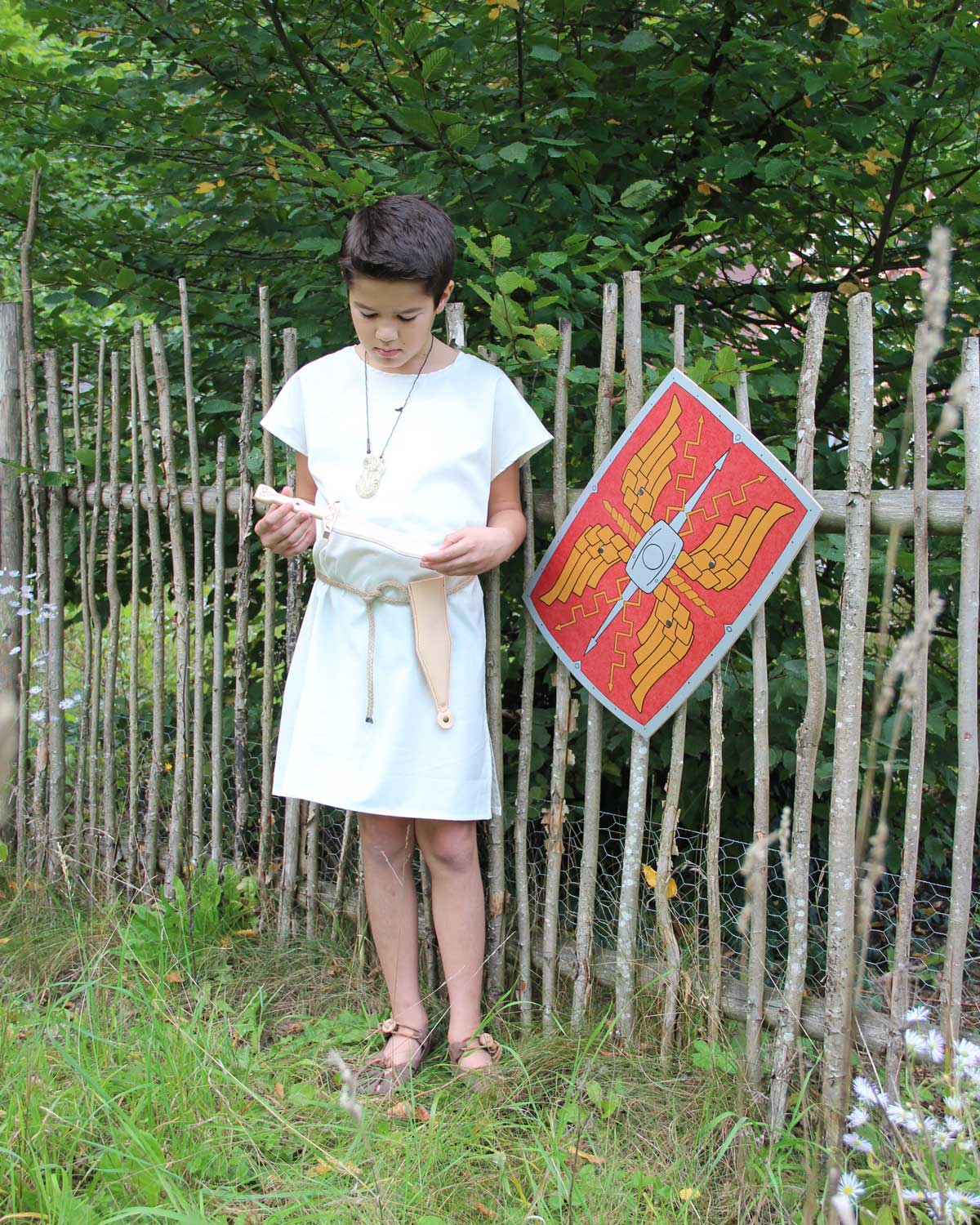 Child wearing the Vah Spartacus Roman Tunic with the red roman alexius shield placed on a fence next to them