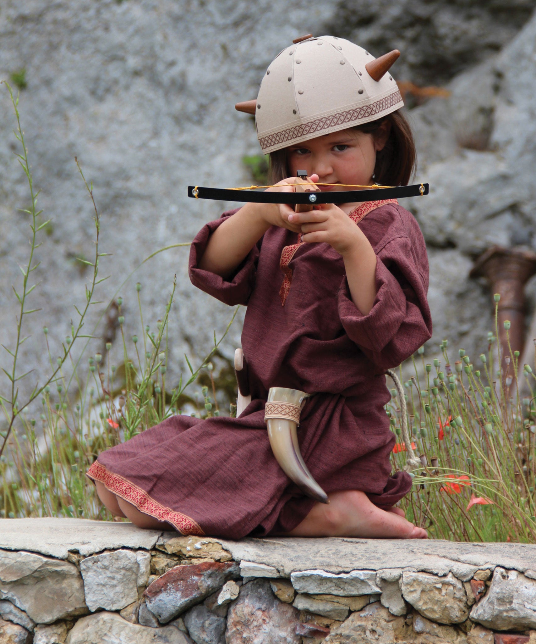 A child in full Viking costume including the Vah Viking Tunic, helmet and drinking horn. The child is playing with a cross bow.