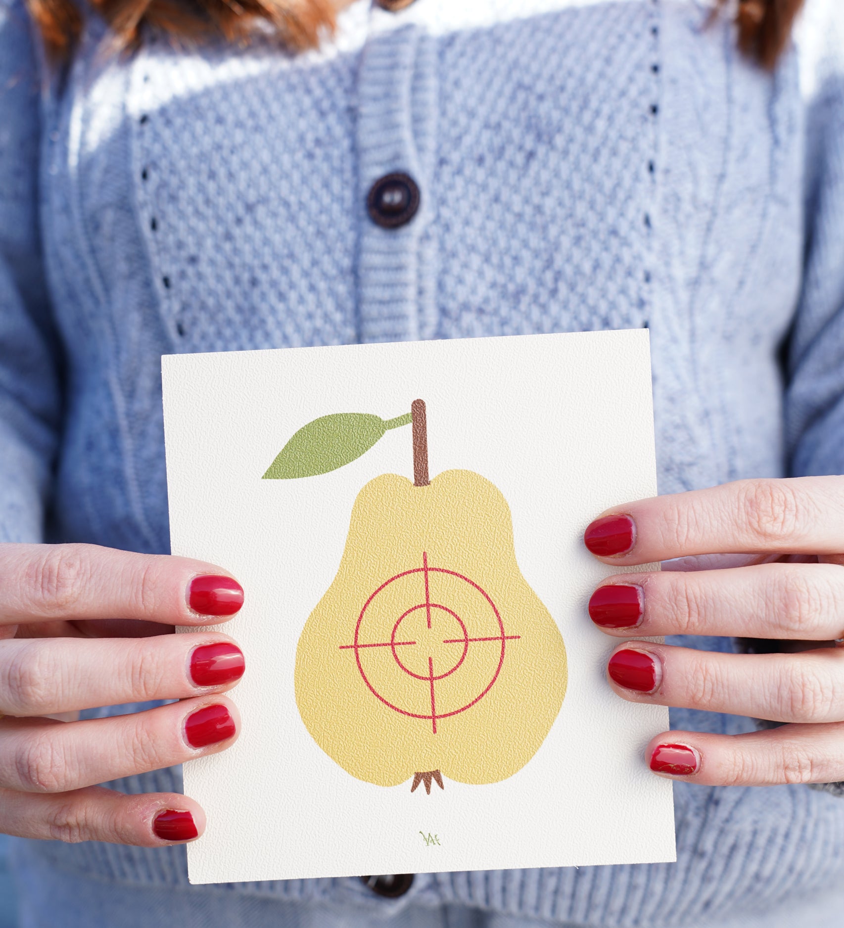 A close up of an an adult's hand holding onto the pear Vah Wooden Fruit Target.