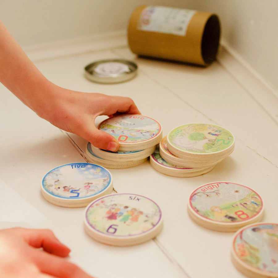 Close up of a childs hand holding the eco-friendly handmade Waldorf family number discs on a white table