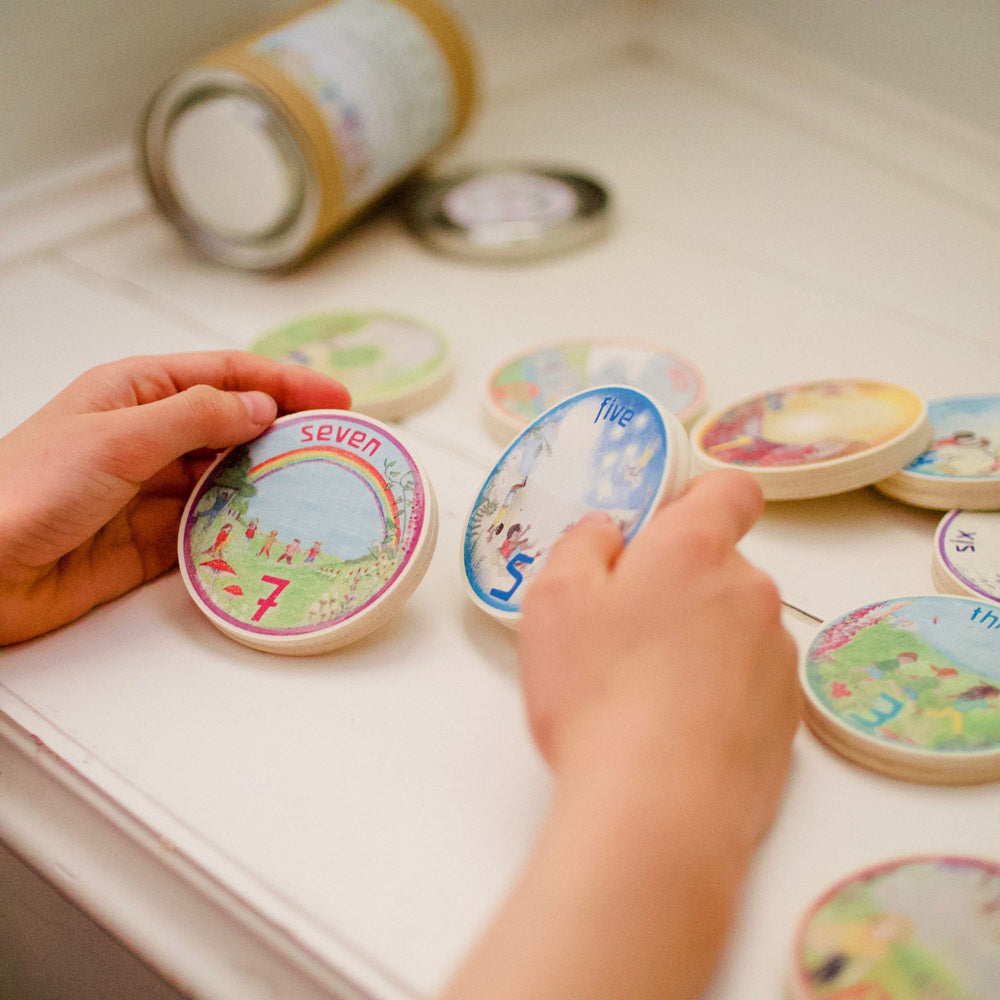 Close up of a childs hands holding the Waldorf family 0-9 number circles on a white table