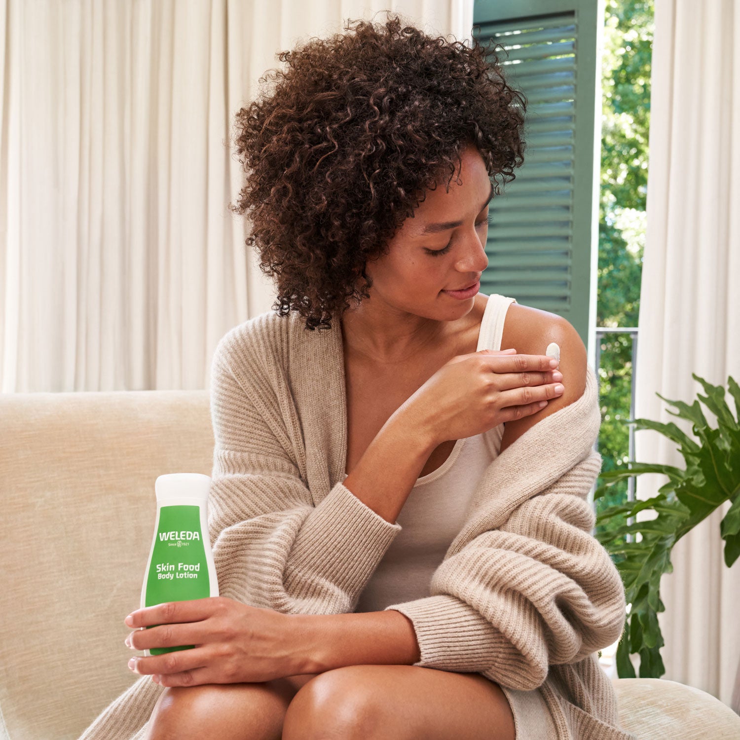 A person applying the Weleda Skin Food Body Lotion to their shoulder