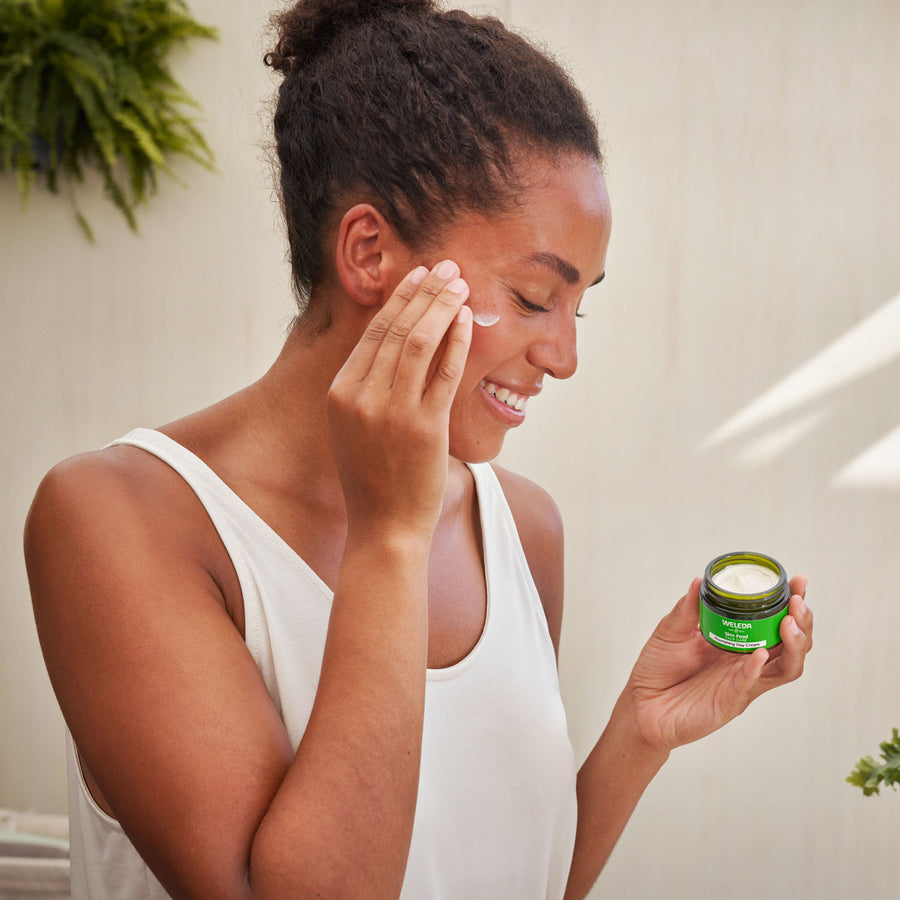 An image of a person applying the Weleda Skin Food Nourishing Day Face Cream to their cheeks