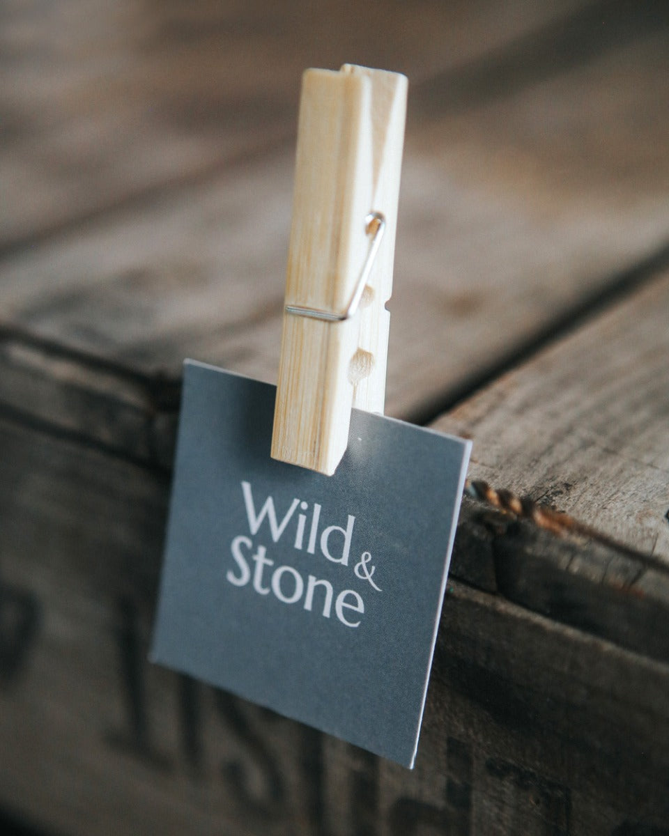 Close up of a Wild and Stone bamboo clothes peg holding a small card square to a wooden table