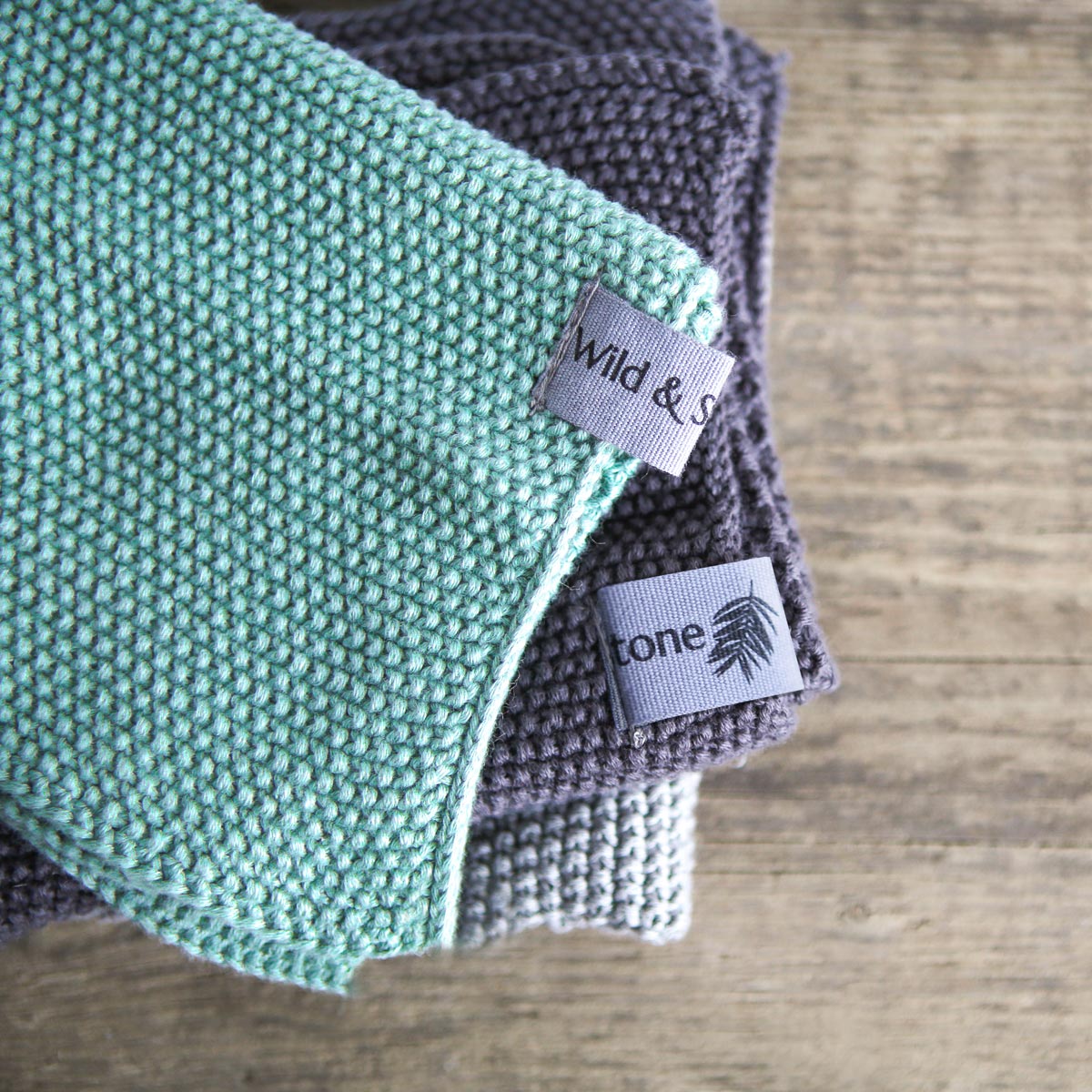 Close up of the textures and labels on the Wild and Stone organic cotton dish cloths on a wooden background