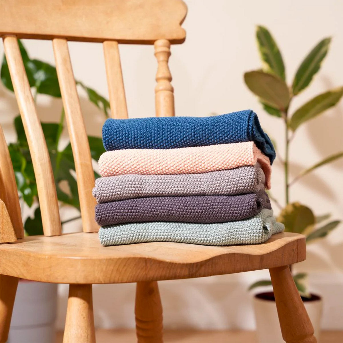 Stack of Wild and Stone organic cotton coloured hand towels on a wooden chair in front of some potted plants