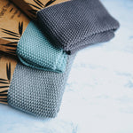 Close up of 3 Wild and Stone organic cotton dish cloths on a white marble background