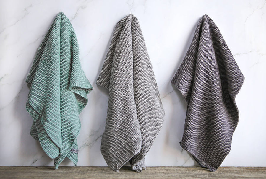 3 Wild and Stone organic cotton hand towels hung up in a line on a white marble background