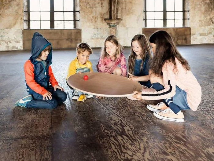 Children rolling a ball on a Wobbel 360 Balance Board with Felt on a wooden floor