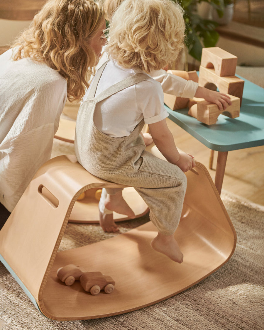 Child sat on top of the Wobbel beech wood Big Up balancing box in front of a blue table