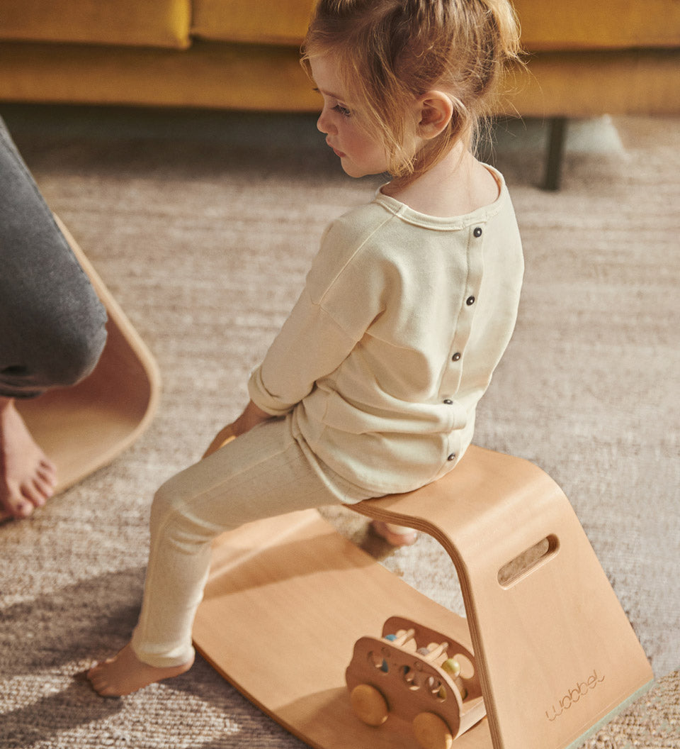 Young girl sat on a Wobbel wooden Up balance box on a grey carpet