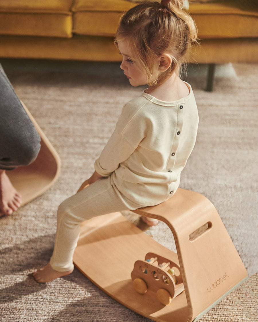 Young girl sat on a Wobbel wooden Up balance box on a grey carpet