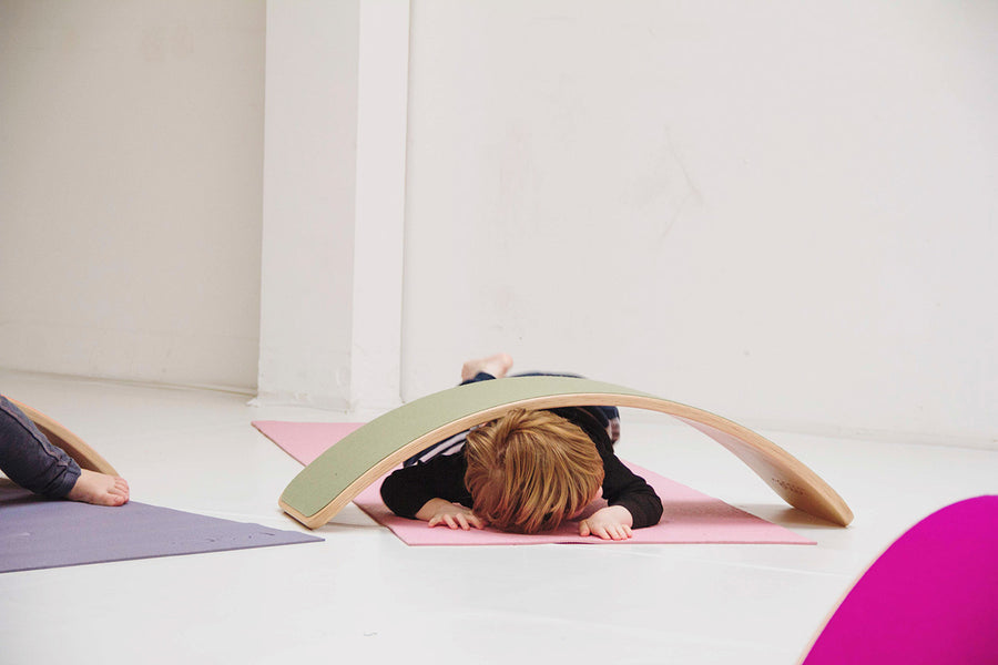 Child crawling underneath a Wobbel Beech Wood balance Board on a yoga mat