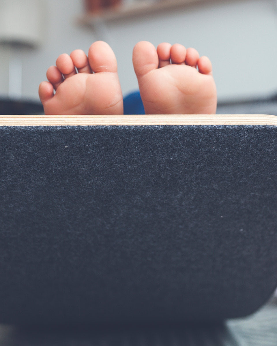 Close up of childs bare feet sticking out of the top of a Wobbel Pro Felt balance board