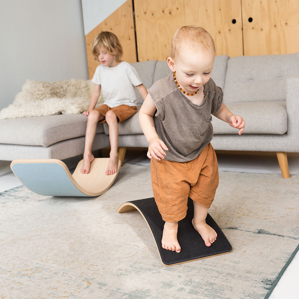 Young children playing on a Wobble Beech Wood Starter wobble board and Wobble Board Felt in a living room