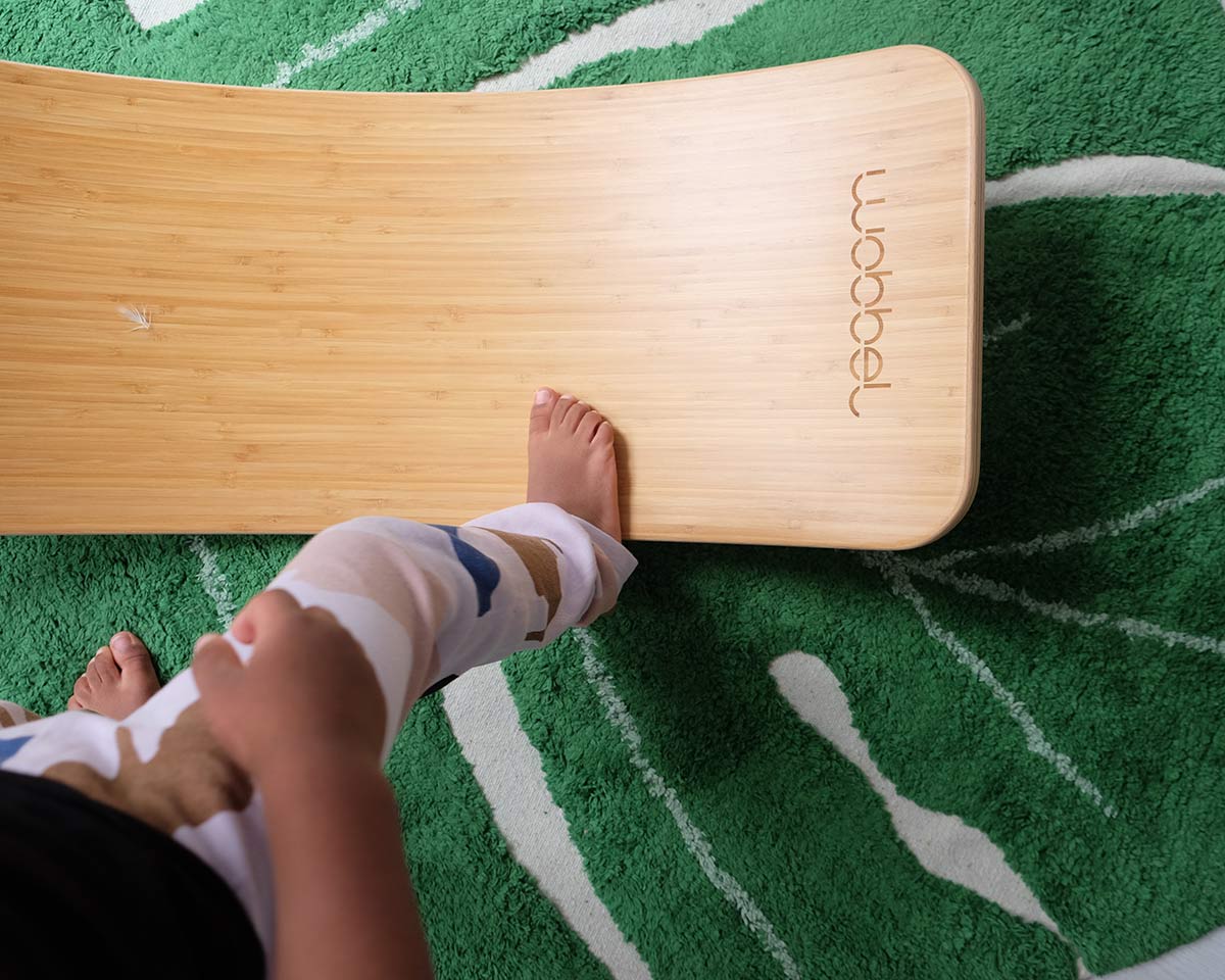 Close up of childs foot on a Wobbel Bamboo balance board on a green leaf carpet