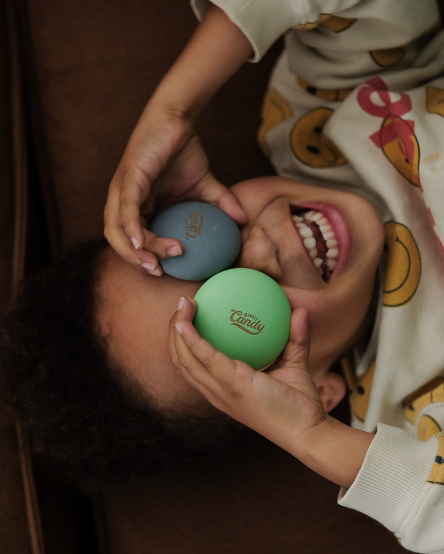 A child happily holding two of the Wobbel Candy Drops up to their eyes. The Candy Drops in the photo are from the Bombai set. Perfect for balancing