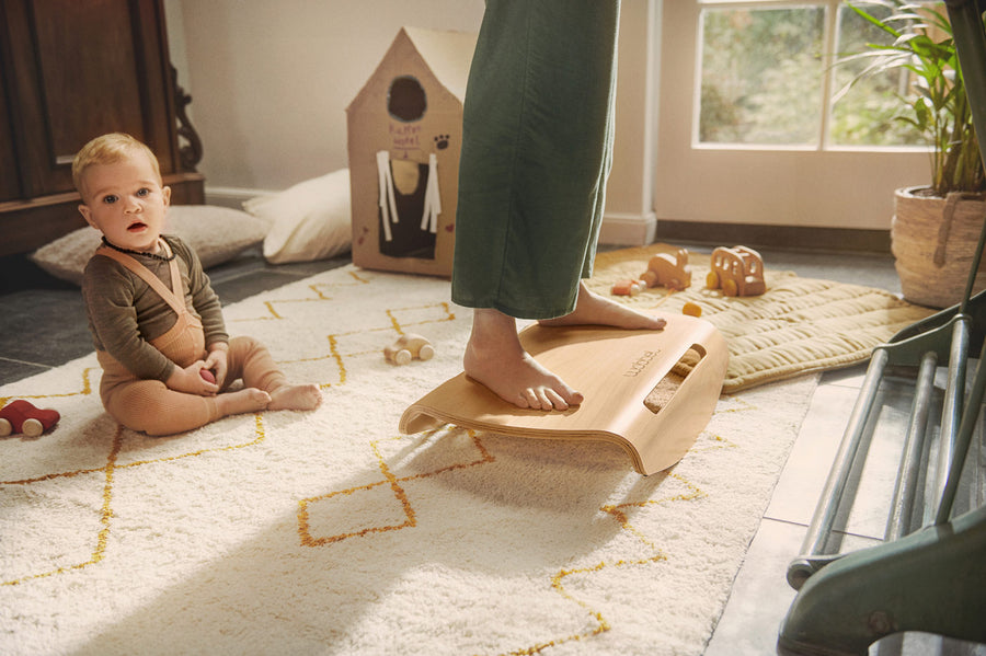 Close up of woman's feet on a Wobbel Sup balance board next to a toddler sat on the floor