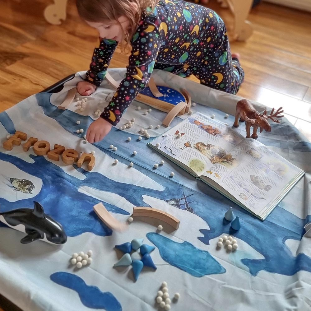 Close up of young girl playing with some wooden toys on the Wonder Cloths Frozen Arctic organic cotton play cloth