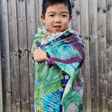 Young boy stood in front of a wooden fence with the large Wonder Cloths organic cotton jungle fabric wrapped around him