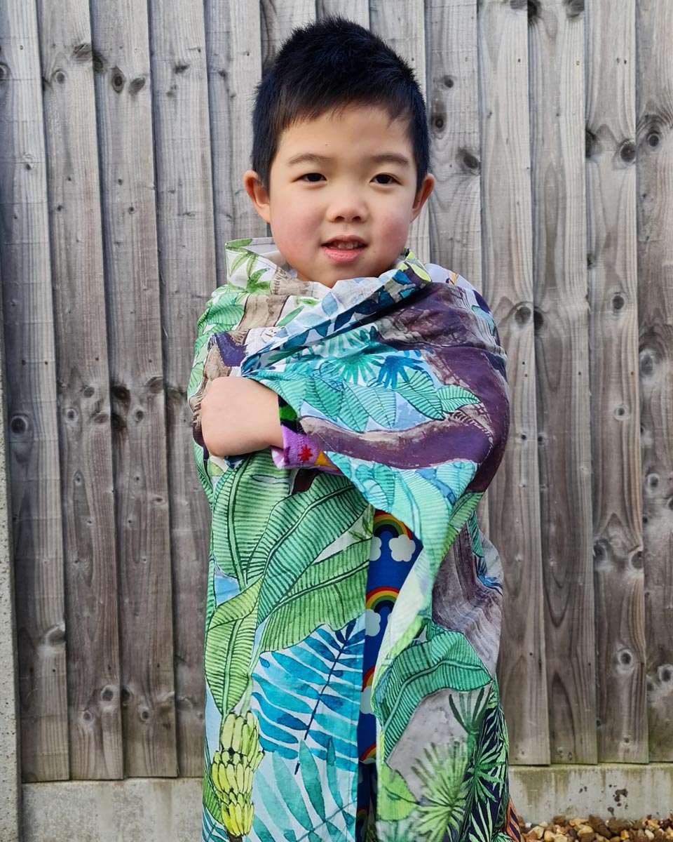 young boy wrapped up in an organic cotton Wonder Cloth in front of a wooden fence