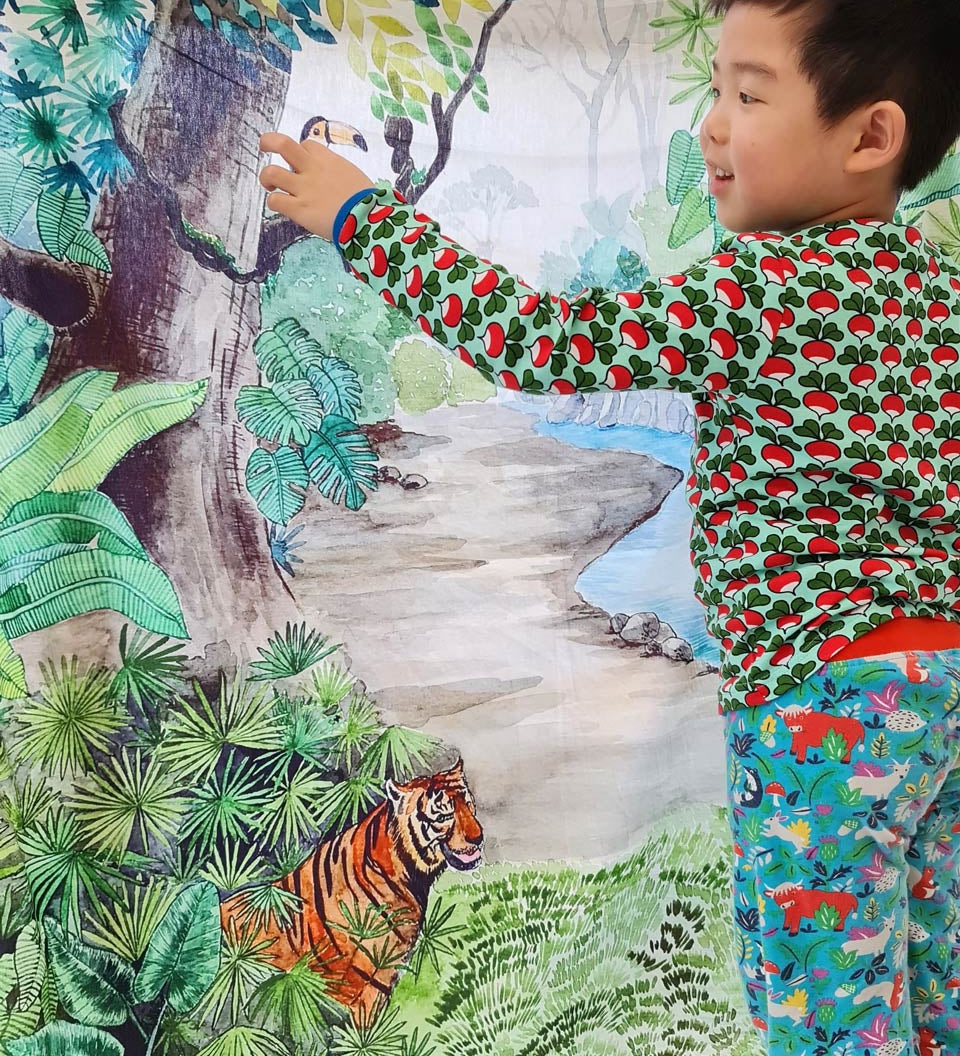 Young boy stood pointing to the Wonder Cloths large jungle playing cloth