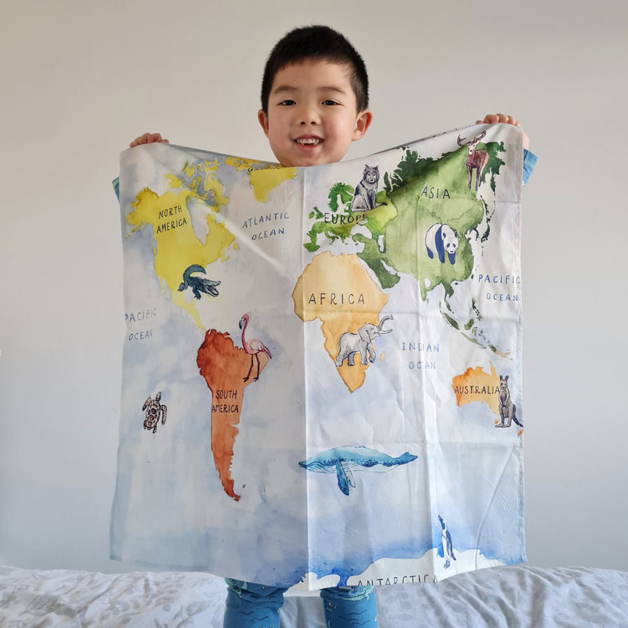 Young boy stood on a bed holding up the Wonder Cloths Our World large learning fabric