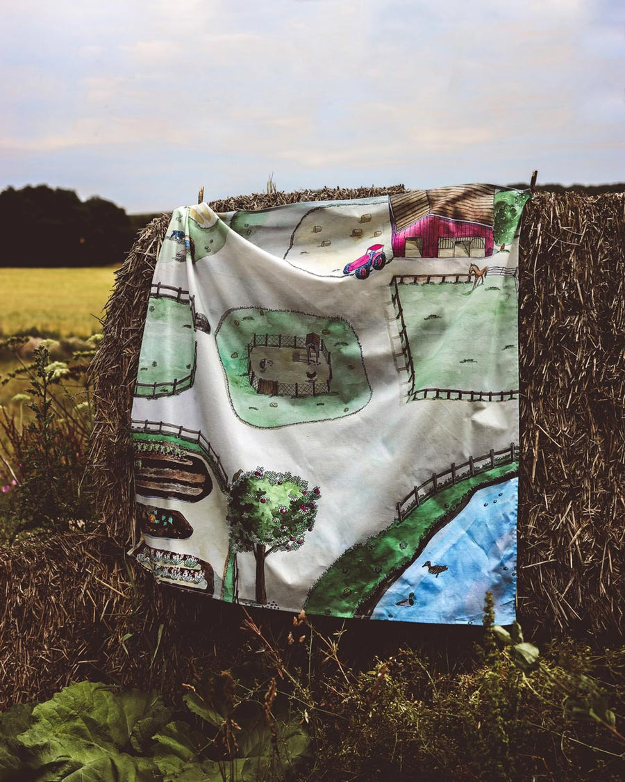 Wondercloths childrens eco-friendly farm print play cloth hanging over a bail of hay in a field